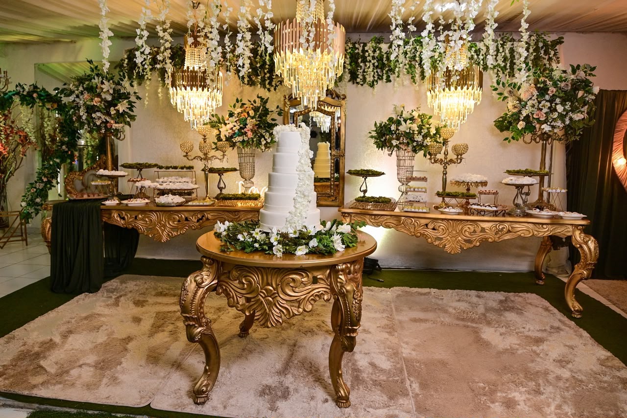 Mesa do bolo decorada com folhagens e flores brancas no salão do Rosa Buffet